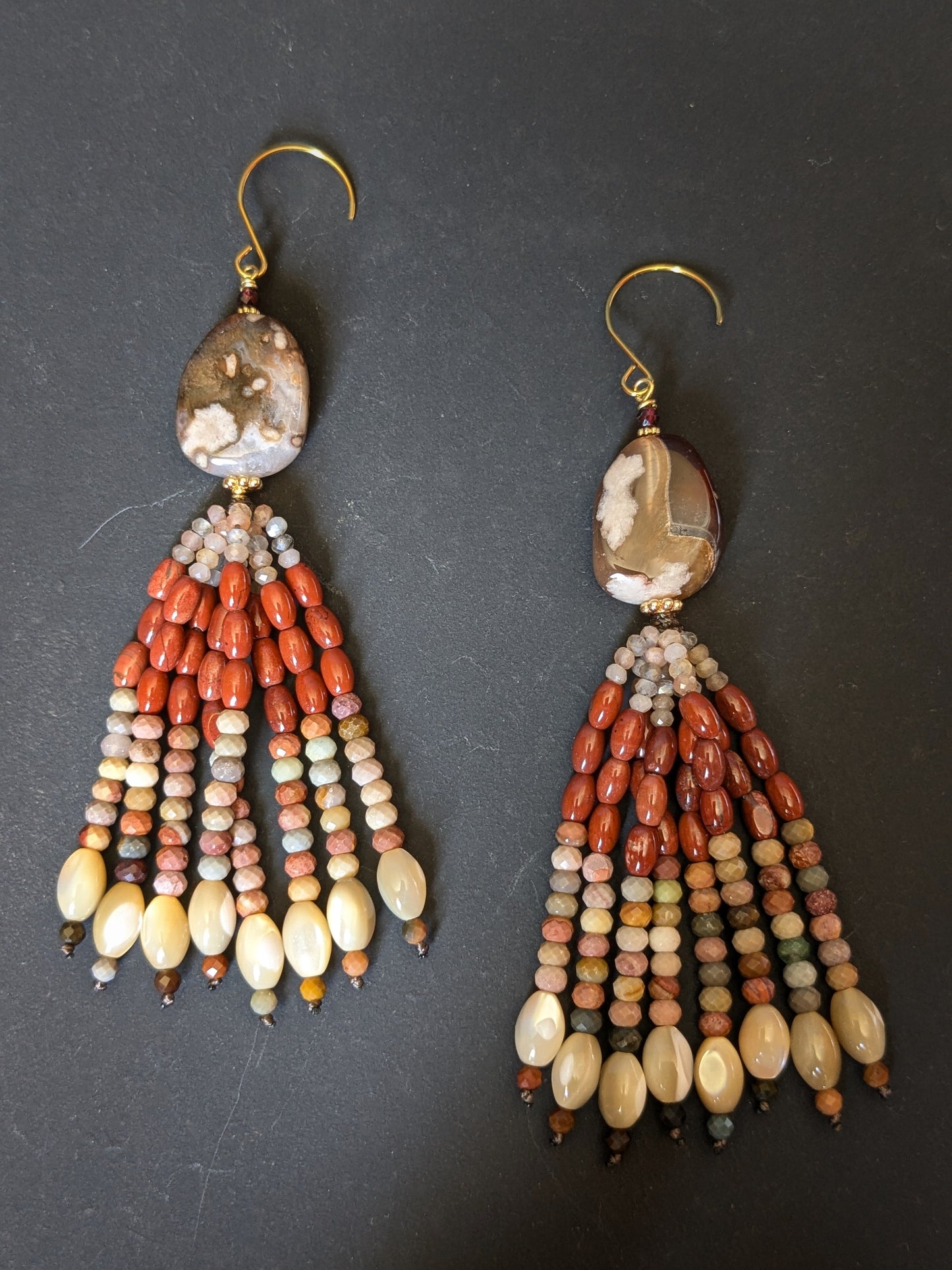 Pendants d'oreilles Asha posés sur un présentoir, agate sakura et tassel pierre de lune pêche et jaspe rouge