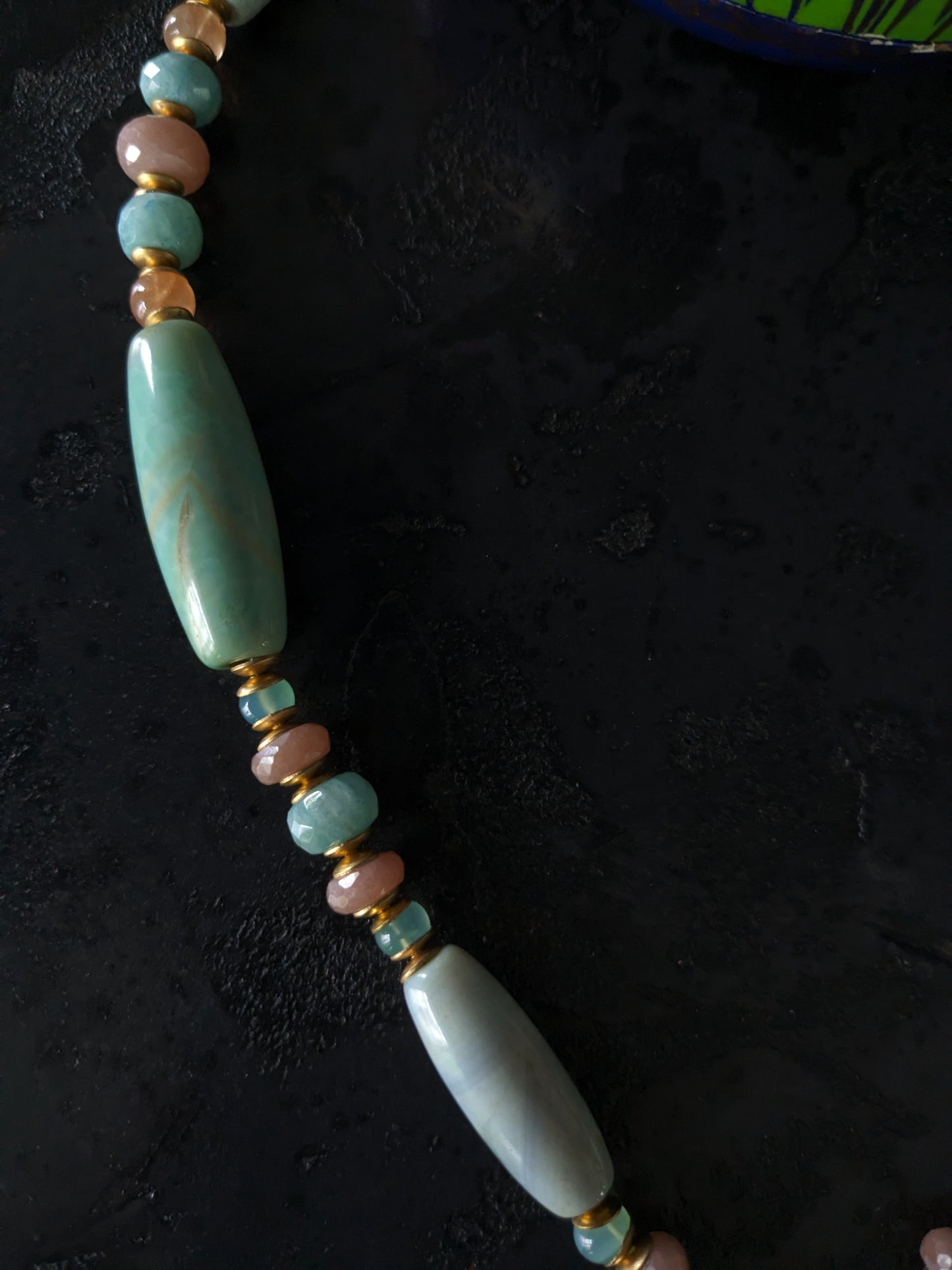 Le collier Bodhisattva de MUDRA est fait à la main avec de l'agate terra aqua, de l'amazonite, de la pierre de lune pêche et de la calcédoine. Il est orné d'une sculpture centrale de bodhisattva délicatement taillée dans du buis.