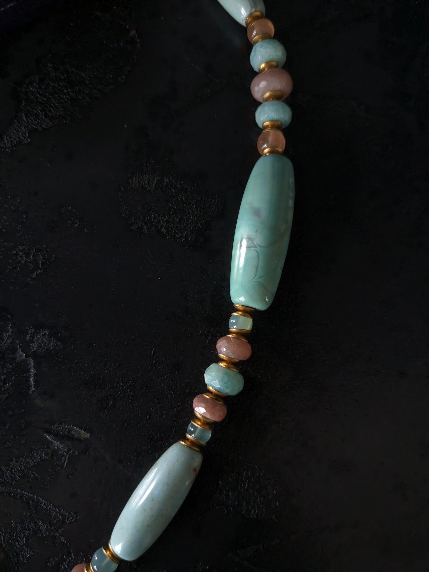 Le collier Bodhisattva de MUDRA est fait à la main avec de l'agate terra aqua, de l'amazonite, de la pierre de lune pêche et de la calcédoine. Il est orné d'une sculpture centrale de bodhisattva délicatement taillée dans du buis.
