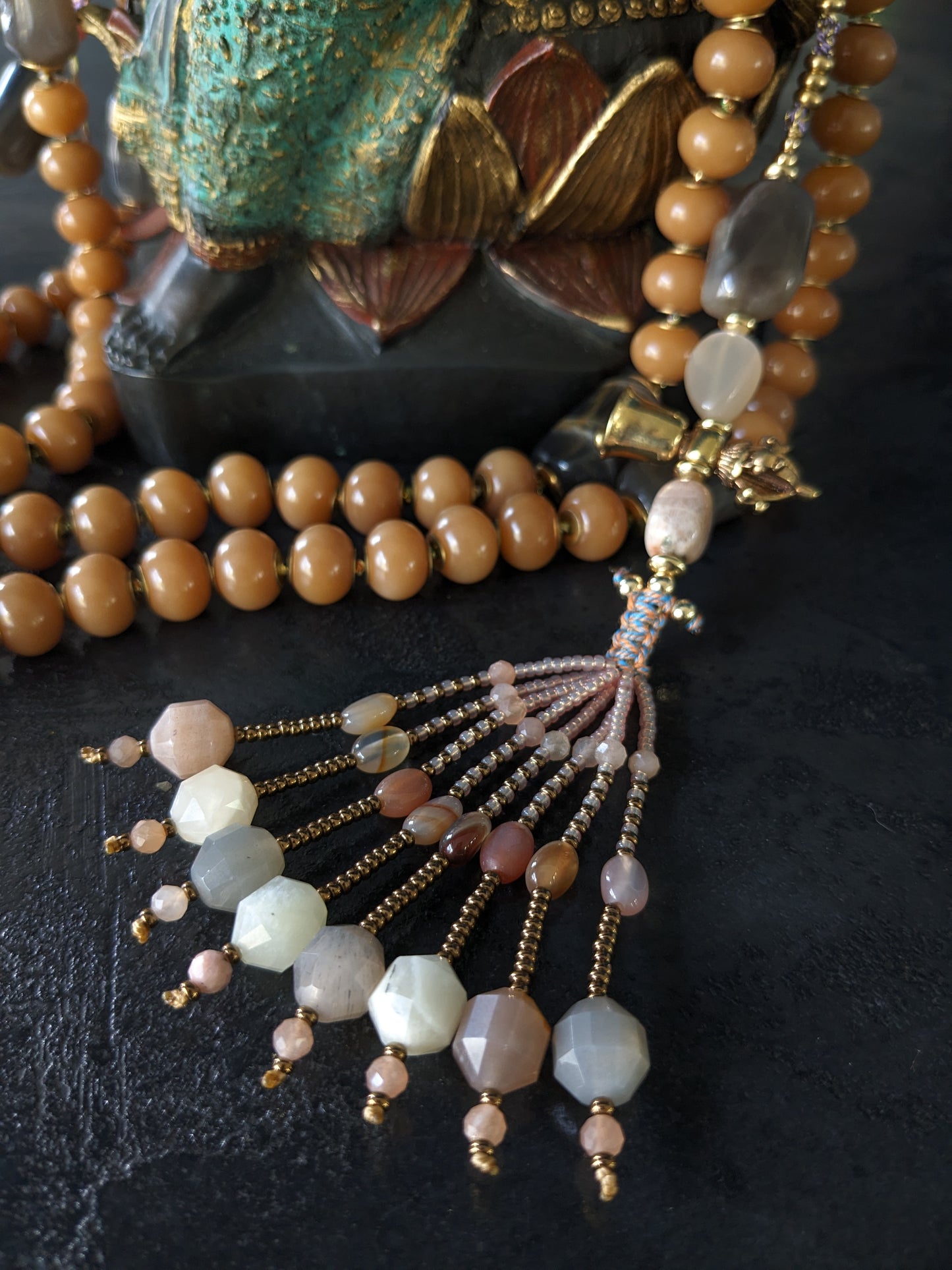 Image d'un magnifique collier Mala Ayodhya, soigneusement placé sur une surface en bois rustique sous une lumière douce et chaleureuse, mettant en valeur ses perles de racine de Bodhi miel naturelles et ses perles de pierre de lune grise. Le design complexe et le savoir-faire artisanal du collier sont mis en évidence.