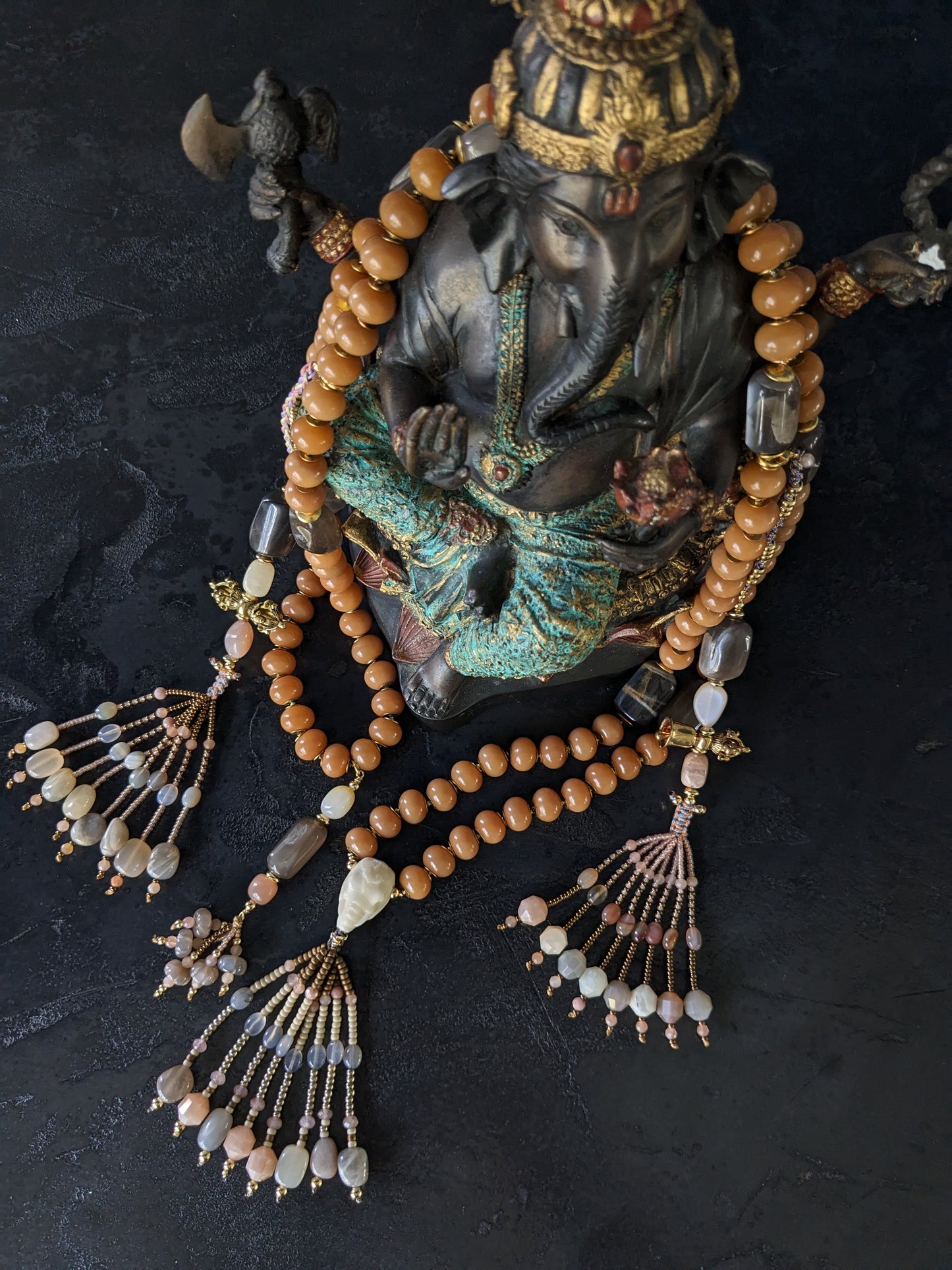 Image d'un magnifique collier Mala Ayodhya, soigneusement placé sur une surface en bois rustique sous une lumière douce et chaleureuse, mettant en valeur ses perles de racine de Bodhi miel naturelles et ses perles de pierre de lune grise. Le design complexe et le savoir-faire artisanal du collier sont mis en évidence.