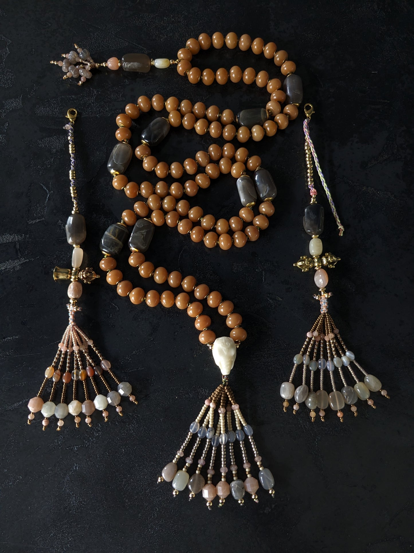 Image d'un magnifique collier Mala Ayodhya, soigneusement placé sur une surface en bois rustique sous une lumière douce et chaleureuse, mettant en valeur ses perles de racine de Bodhi miel naturelles et ses perles de pierre de lune grise. Le design complexe et le savoir-faire artisanal du collier sont mis en évidence.