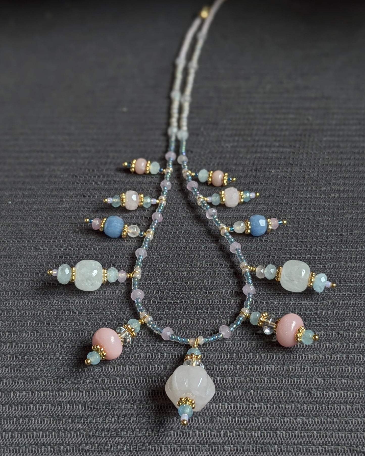 Harmonie de minéraux bleus et roses pour le collier unique Tanisha, présenté sur un support naturel.