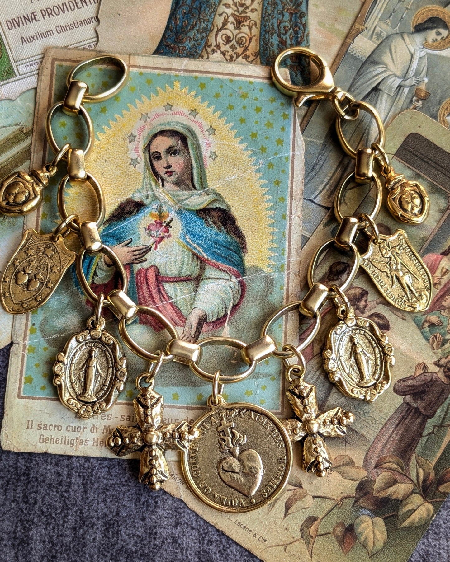 Détail des finitions dorées sur la médaille Saint Michel, les croix et les milagros du bracelet Gloria, révélant le contraste avec la maille épurée et géométrique.