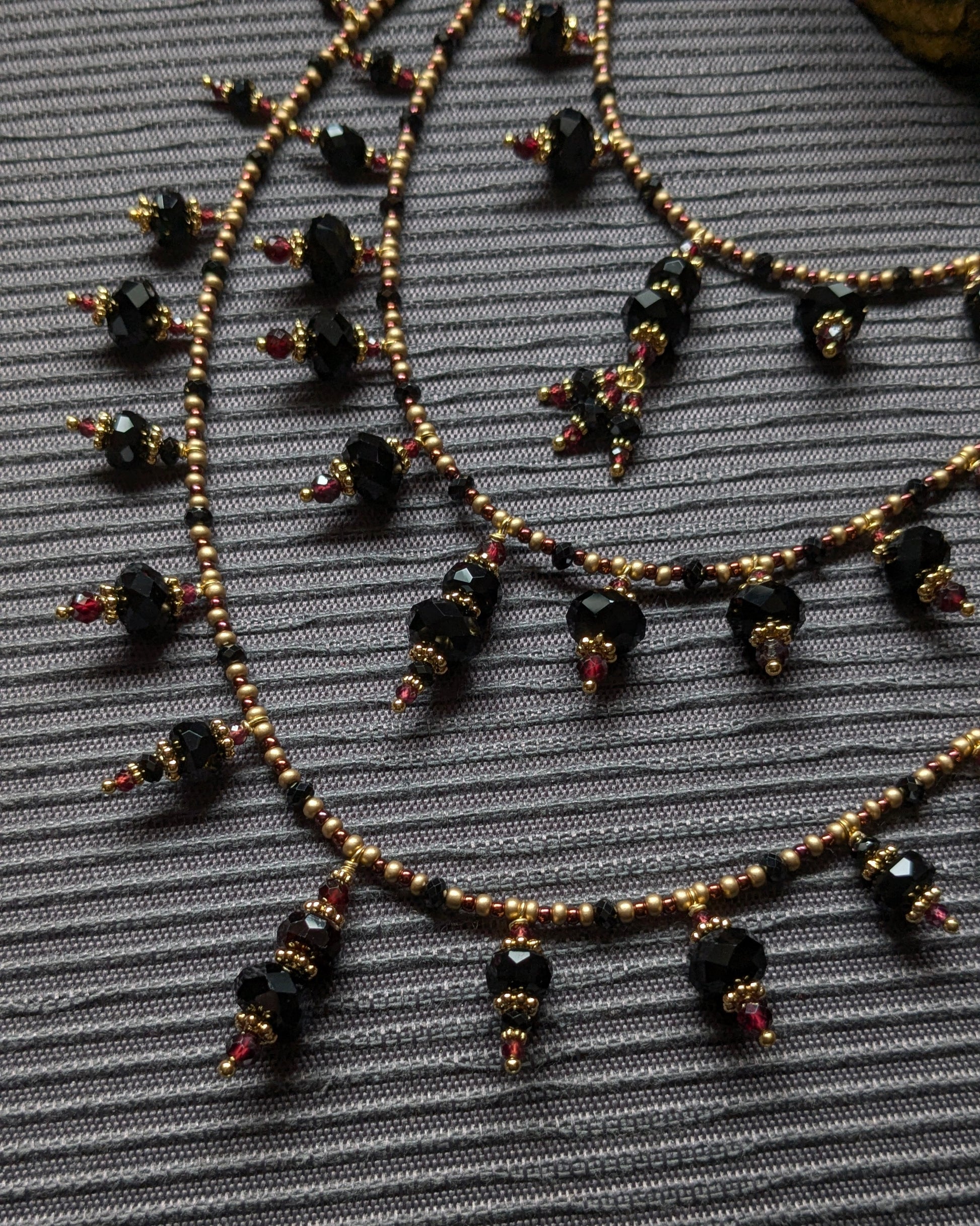 Mouvement fluide des breloques et des franges minérales noires et rouges du collier Aarivya.