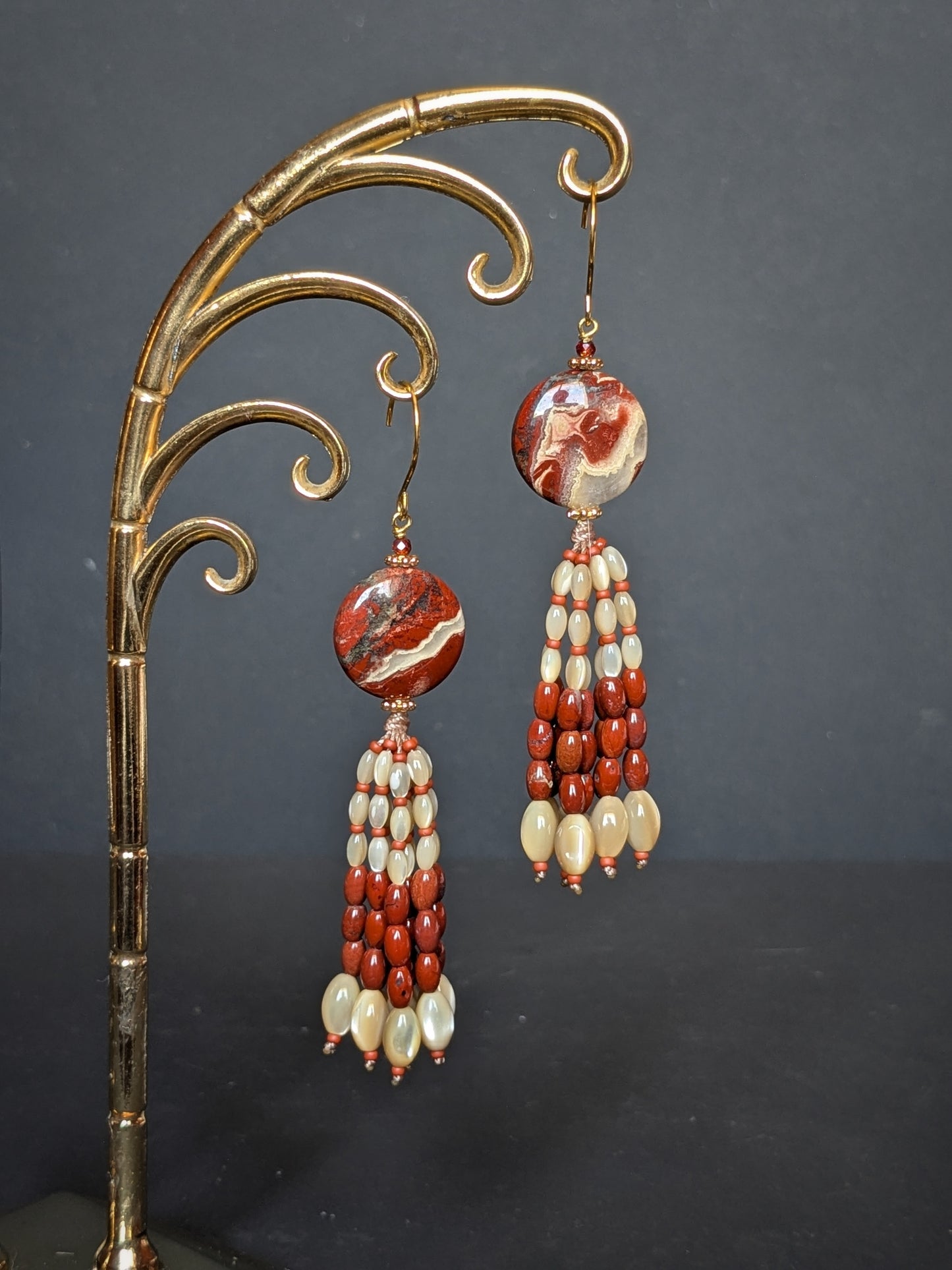 Pendants d'oreilles Amara posés sur un présentoir, perle de jaspe rouge et tassel en nacre de trochus