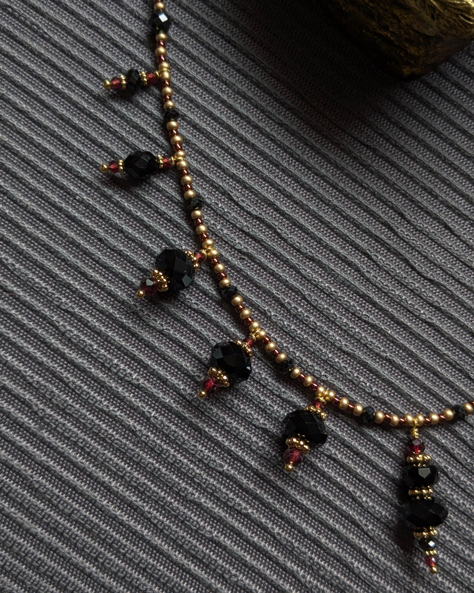 Détail des franges irrégulières d'onyx facetté et de tourmaline noire réagissant à la lumière sur le collier Bhavika.