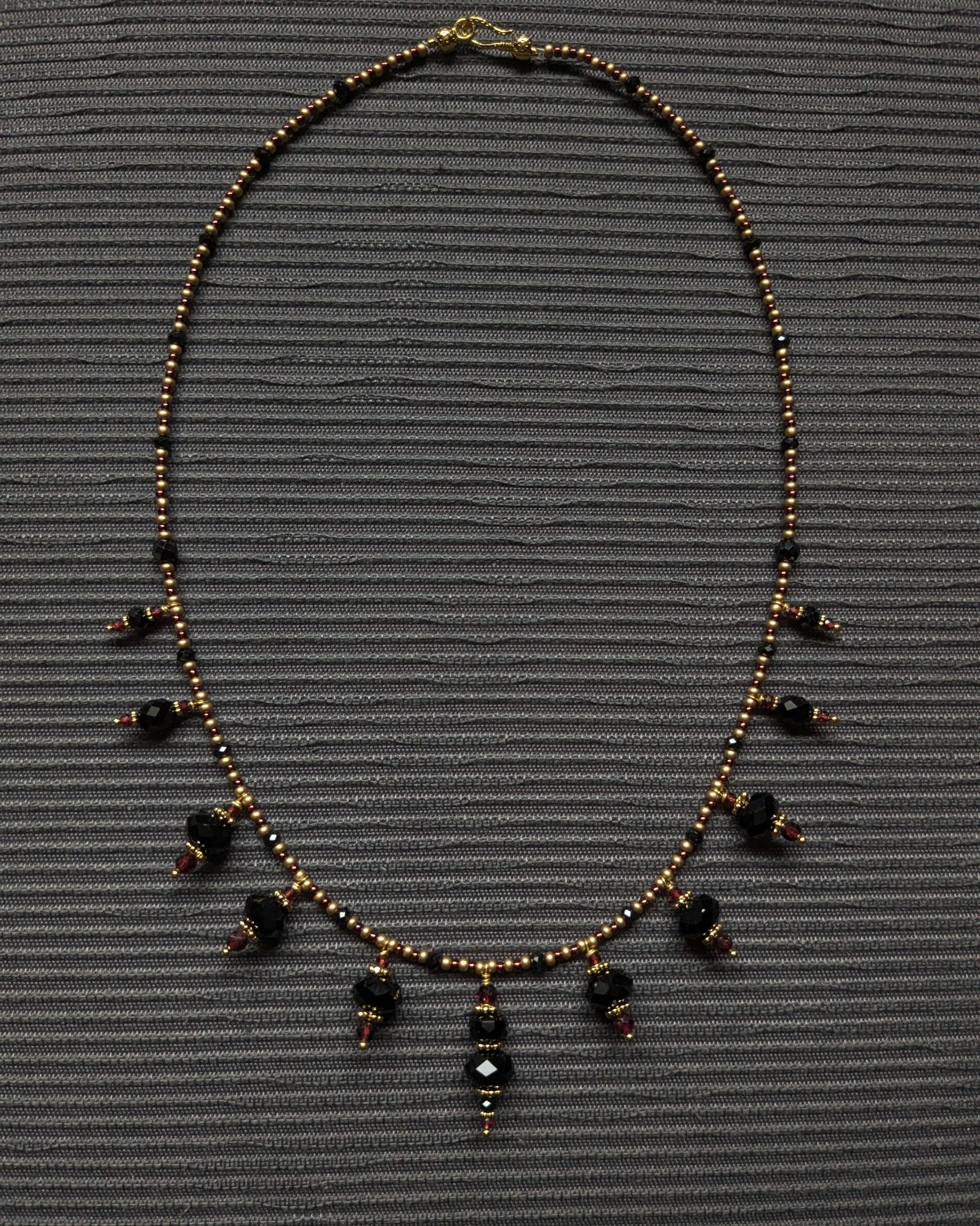 Collier fin Bhavika (50 cm) composé de breloques en pierres noires sur un fil de rocailles bronze et bordeaux.