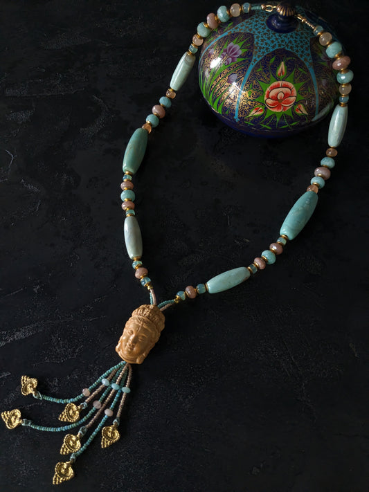 Le collier Bodhisattva de MUDRA est fait à la main avec de l'agate terra aqua, de l'amazonite, de la pierre de lune pêche et de la calcédoine. Il est orné d'une sculpture centrale de bodhisattva délicatement taillée dans du buis. 