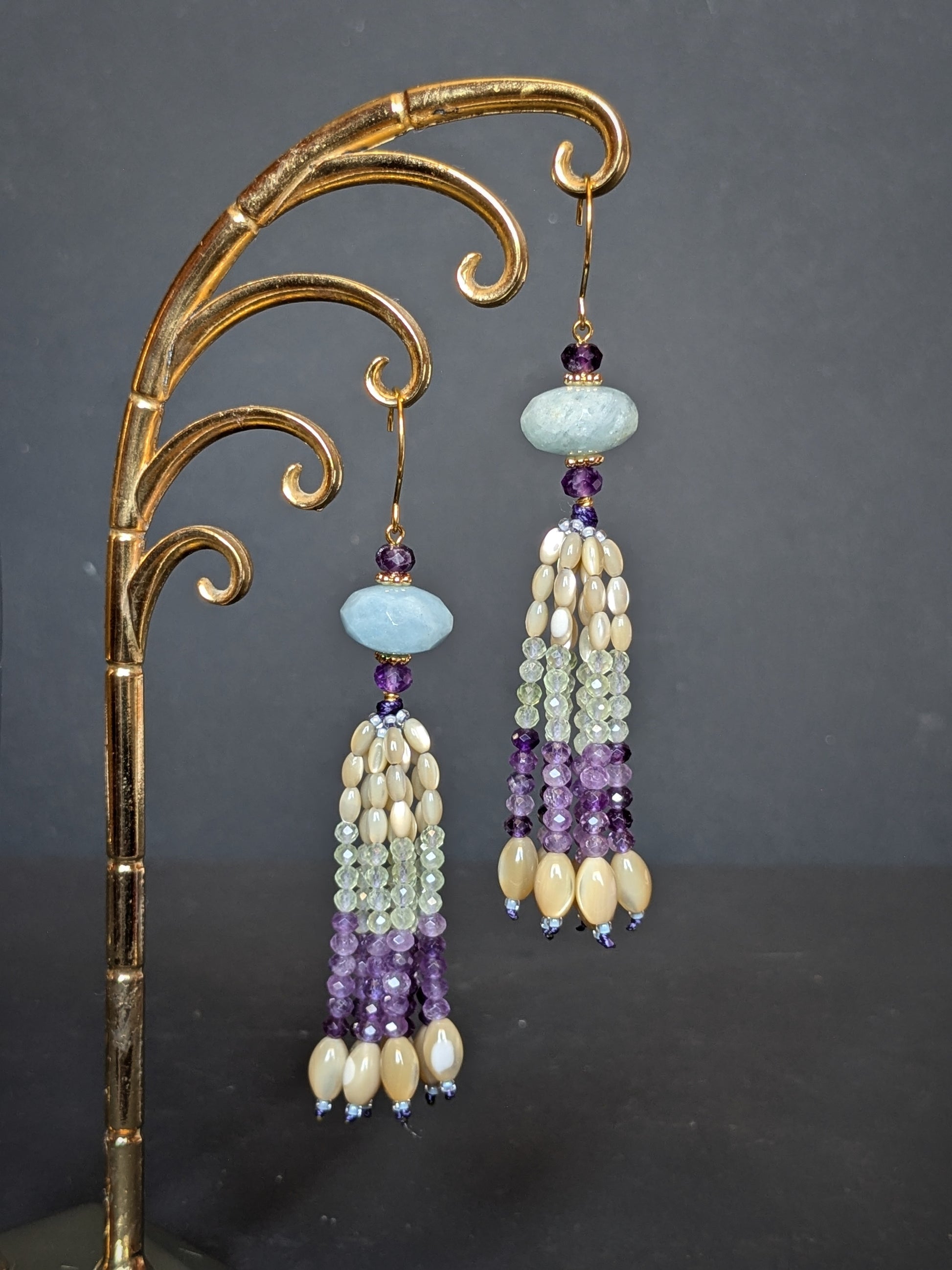 Pendants d'oreilles Ishika suspendus sur un présentoir doré, aigue-marine et améthyste en tête, tassel nacre de trochus