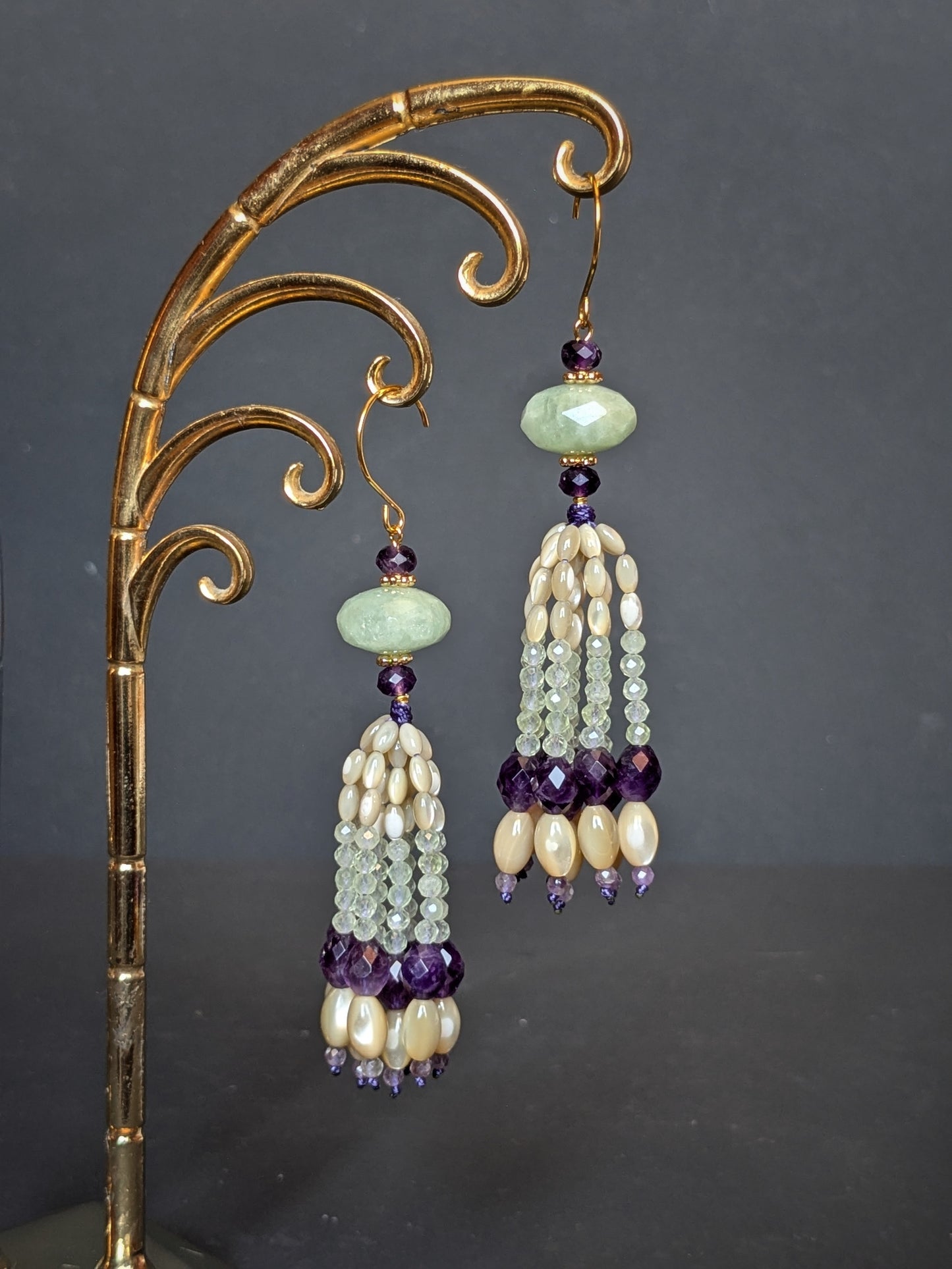 Pendants d'oreilles Kalyani suspendus sur un présentoir doré, aigue-marine et améthyste en tête, tassel nacre de trochus et améthyste intense