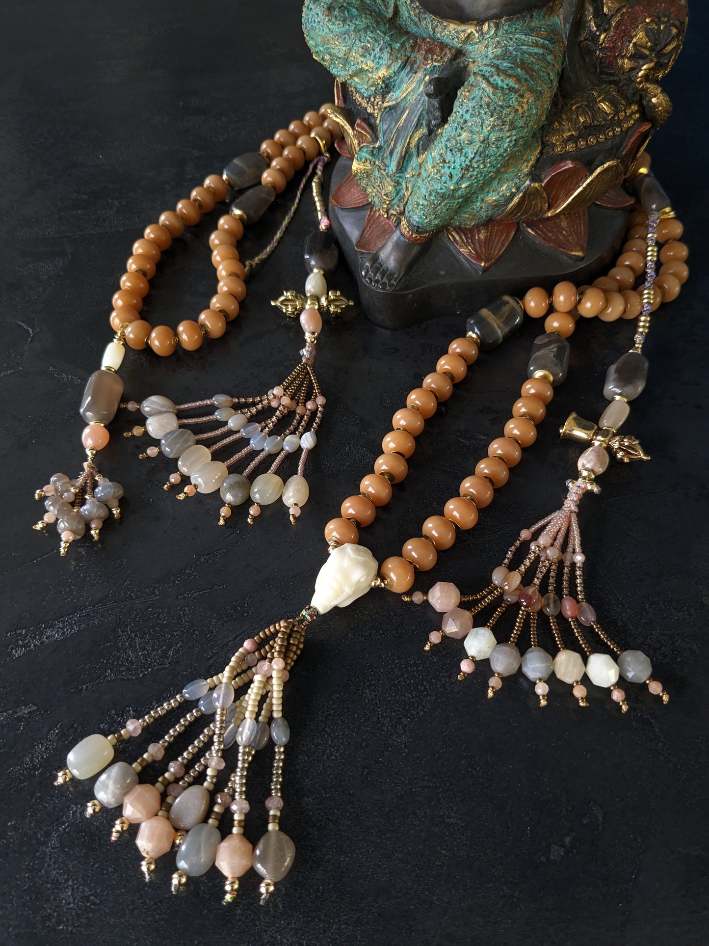 Image d'un magnifique collier Mala Ayodhya, soigneusement placé sur une surface en bois rustique sous une lumière douce et chaleureuse, mettant en valeur ses perles de racine de Bodhi miel naturelles et ses perles de pierre de lune grise. Le design complexe et le savoir-faire artisanal du collier sont mis en évidence.
