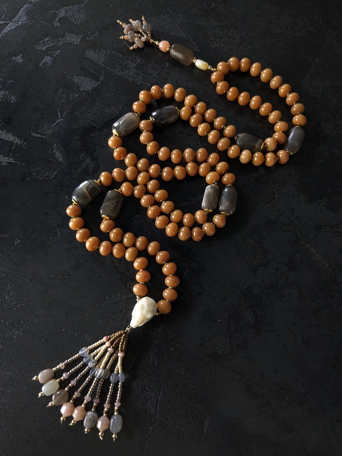 Image d'un magnifique collier Mala Ayodhya, soigneusement placé sur une surface en bois rustique sous une lumière douce et chaleureuse, mettant en valeur ses perles de racine de Bodhi miel naturelles et ses perles de pierre de lune grise. Le design complexe et le savoir-faire artisanal du collier sont mis en évidence.
