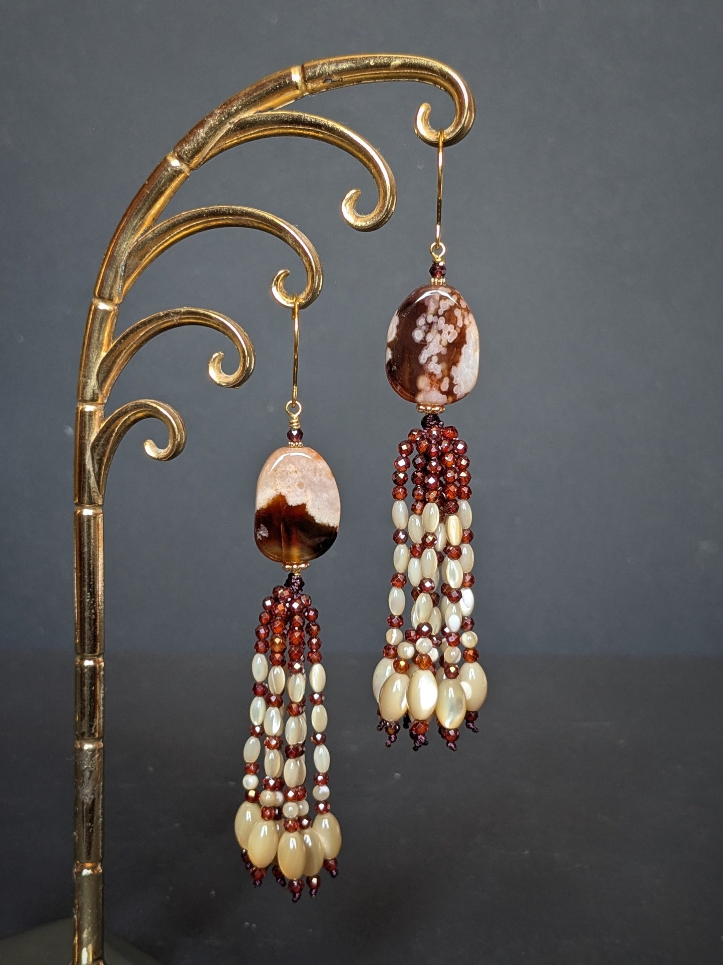 Pendants d'oreilles Mohini posés sur un présentoir, agate sakura acajou et tassel de grenats