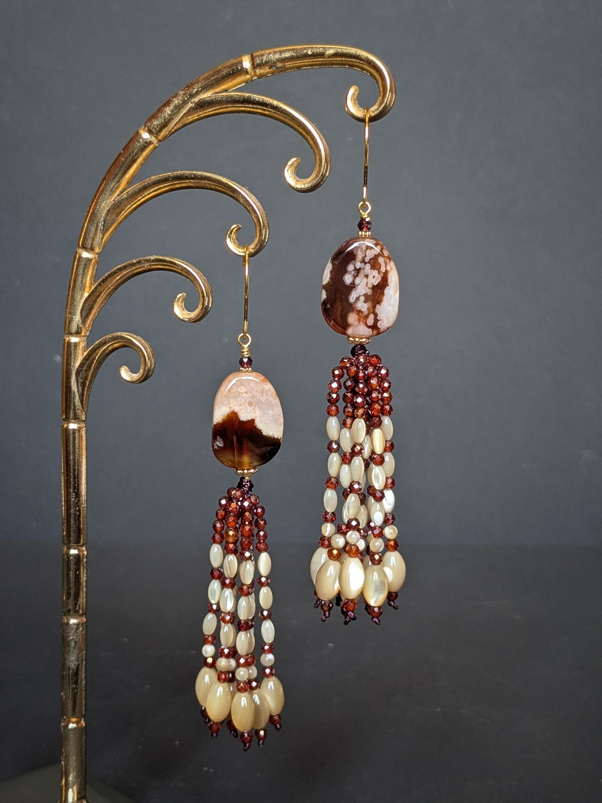 Pendants d'oreilles Mohini posés sur un présentoir, agate sakura acajou et tassel de grenats