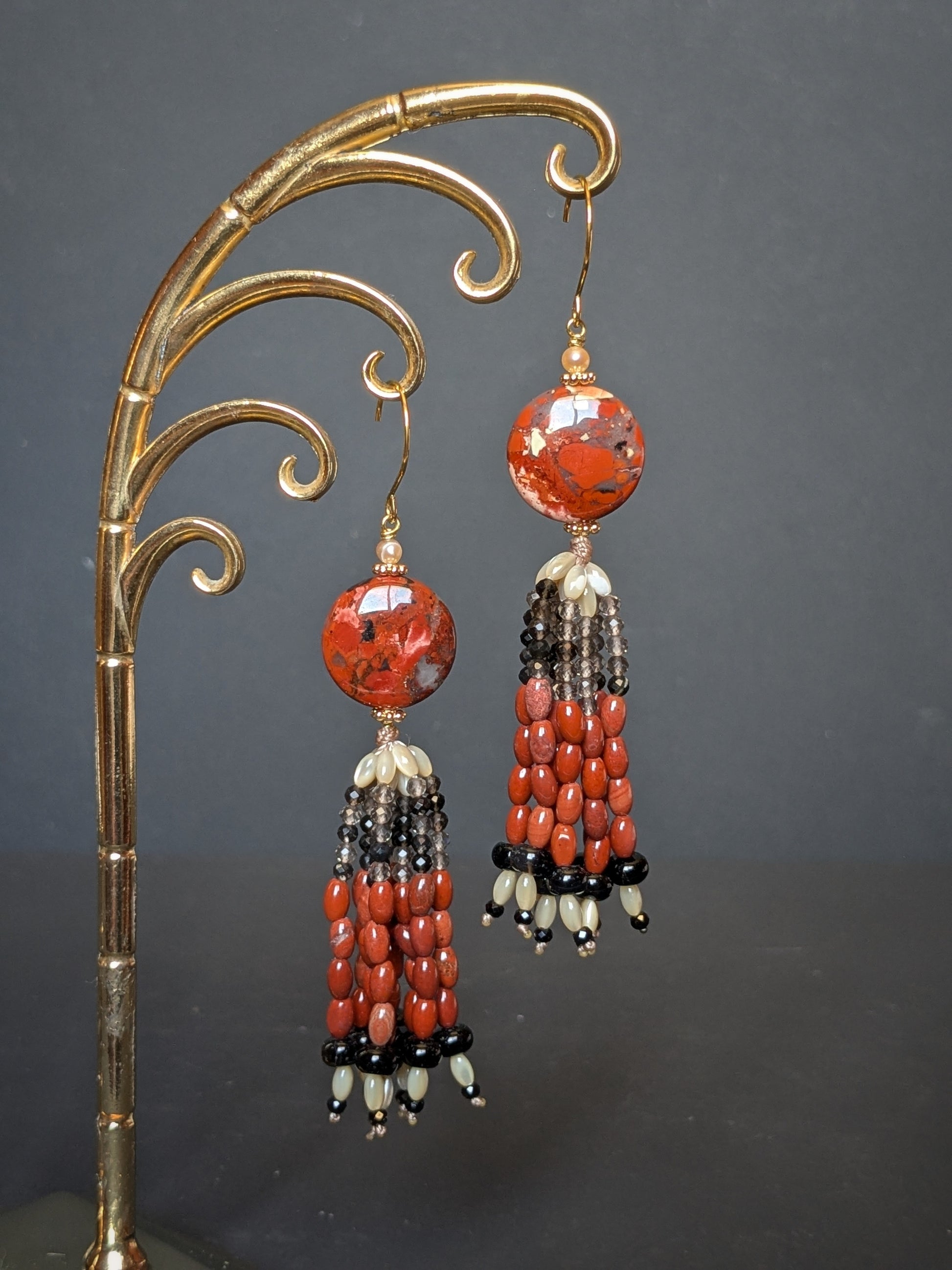 Pendants d'oreilles Ojal posés sur un présentoir, disque de jaspe rouge et tassel en onyx et spinelle noir
