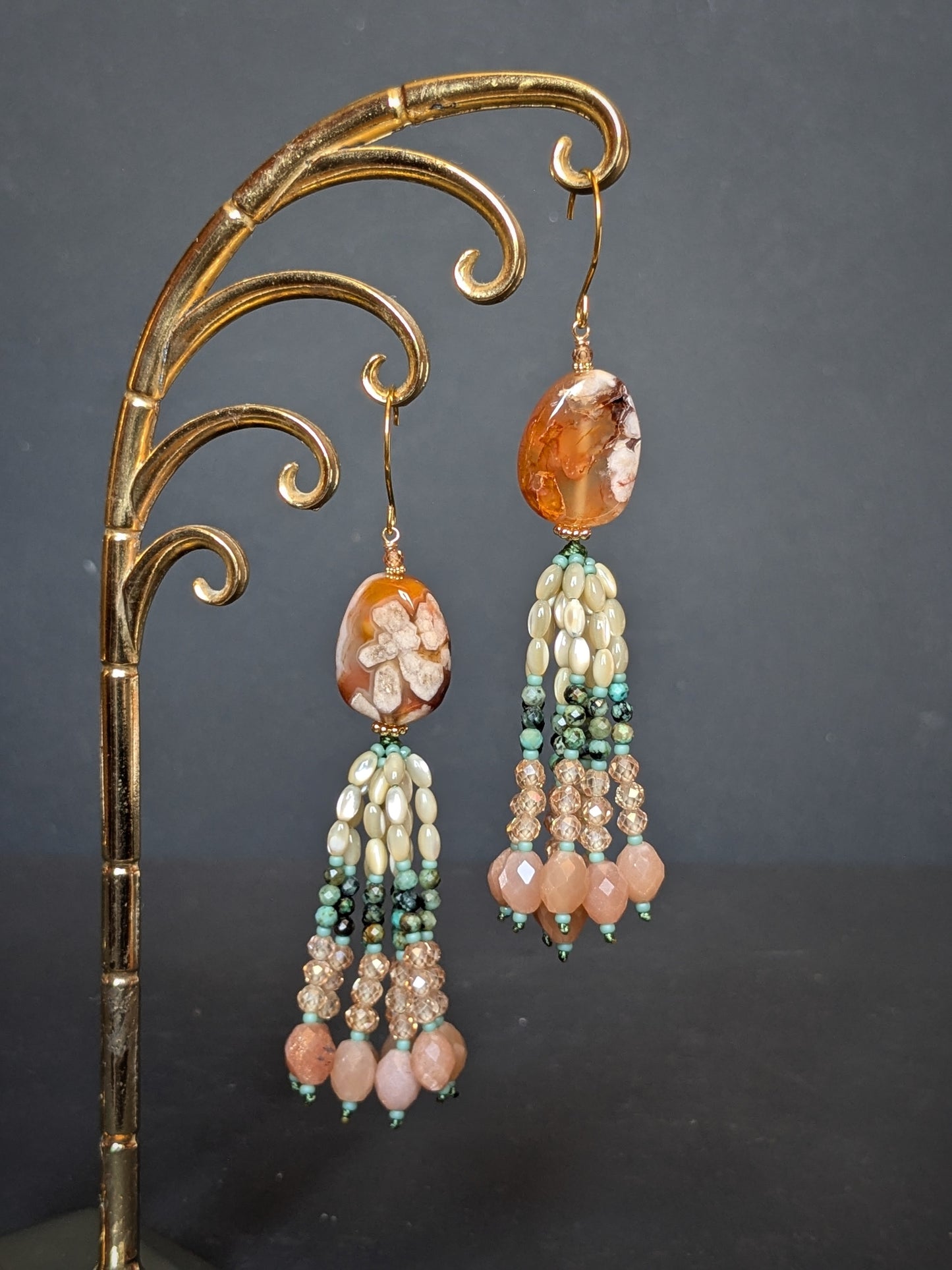 Pendants d'oreilles Sundari posés sur un présentoir, agate sakura orangée et tassel turquoise africaine et pêche