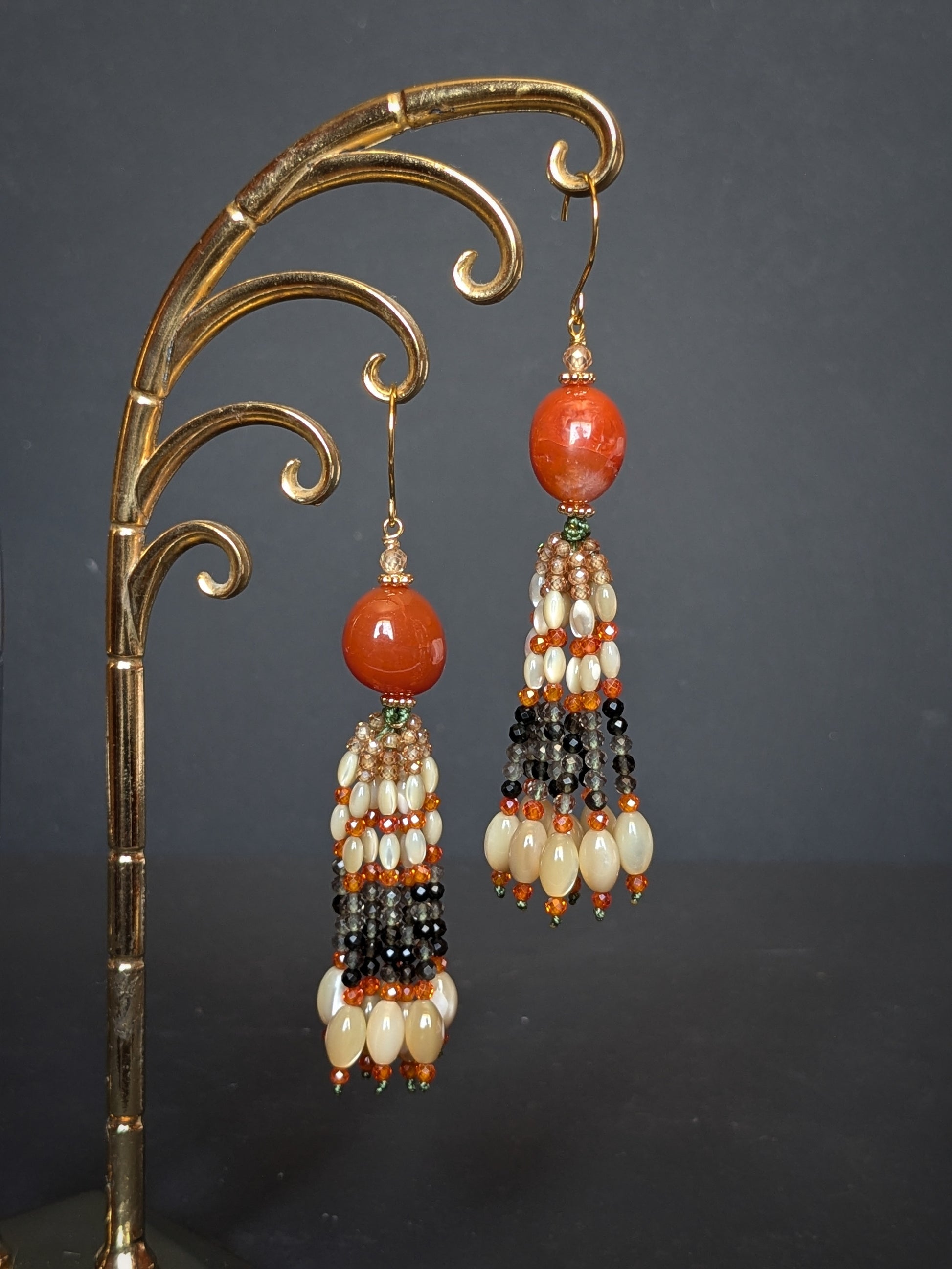 Pendants d'oreilles Zoya posés sur un présentoir, agate du Botswana orange brûlé et tassel dégradé vers le gris fumé