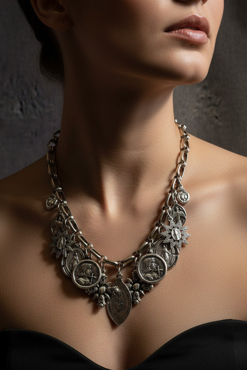 Collier porté Manifesto de Mudra, un plastron baroque et rock au volume maximaliste habillant le décolleté avec une accumulation de médailles sacrées patinées.