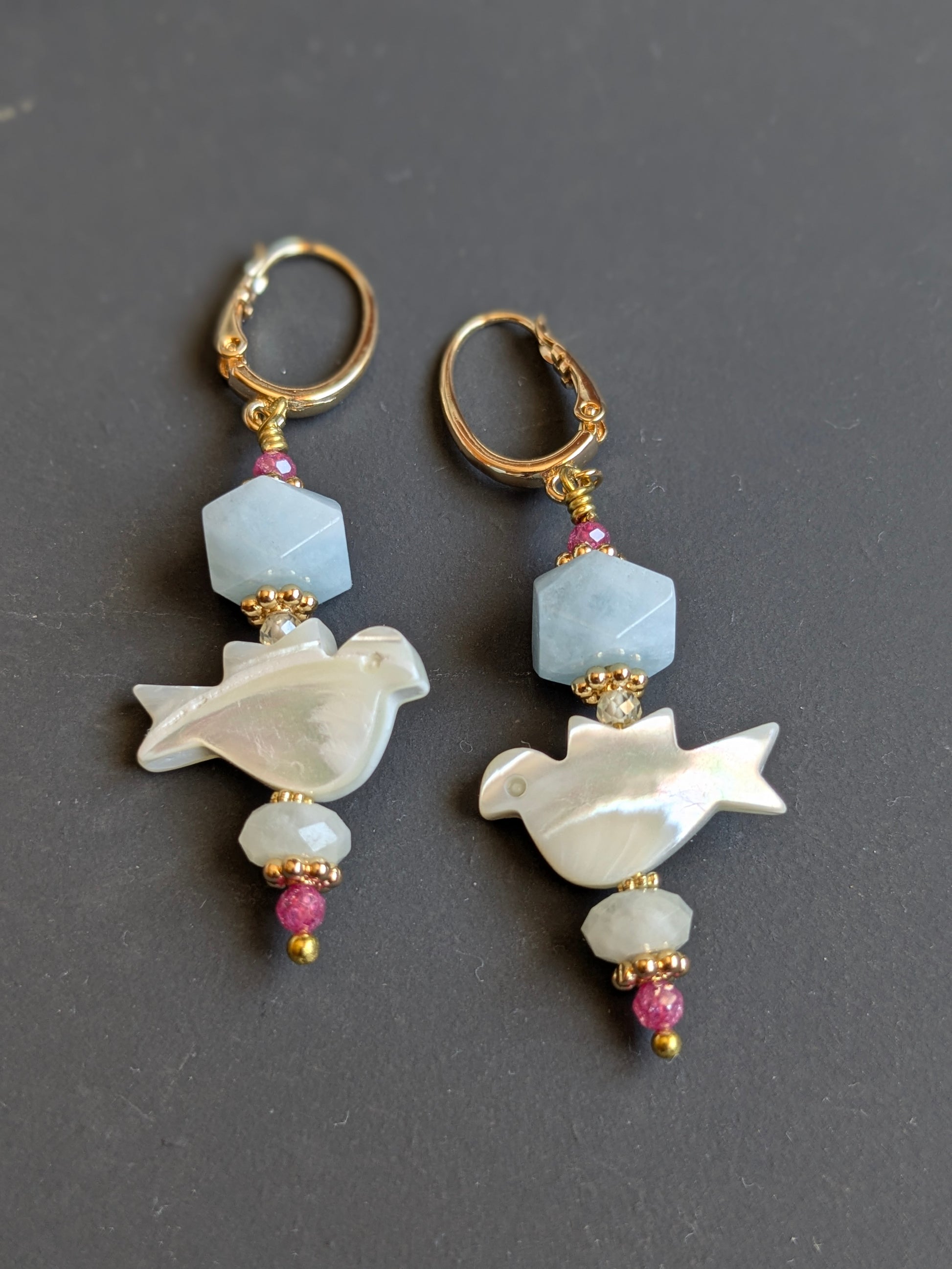 Détail de la colombe sculptée à la main en nacre de trochus sur les boucles d'oreilles Ananya, avec aigue-marine et zircon rose
