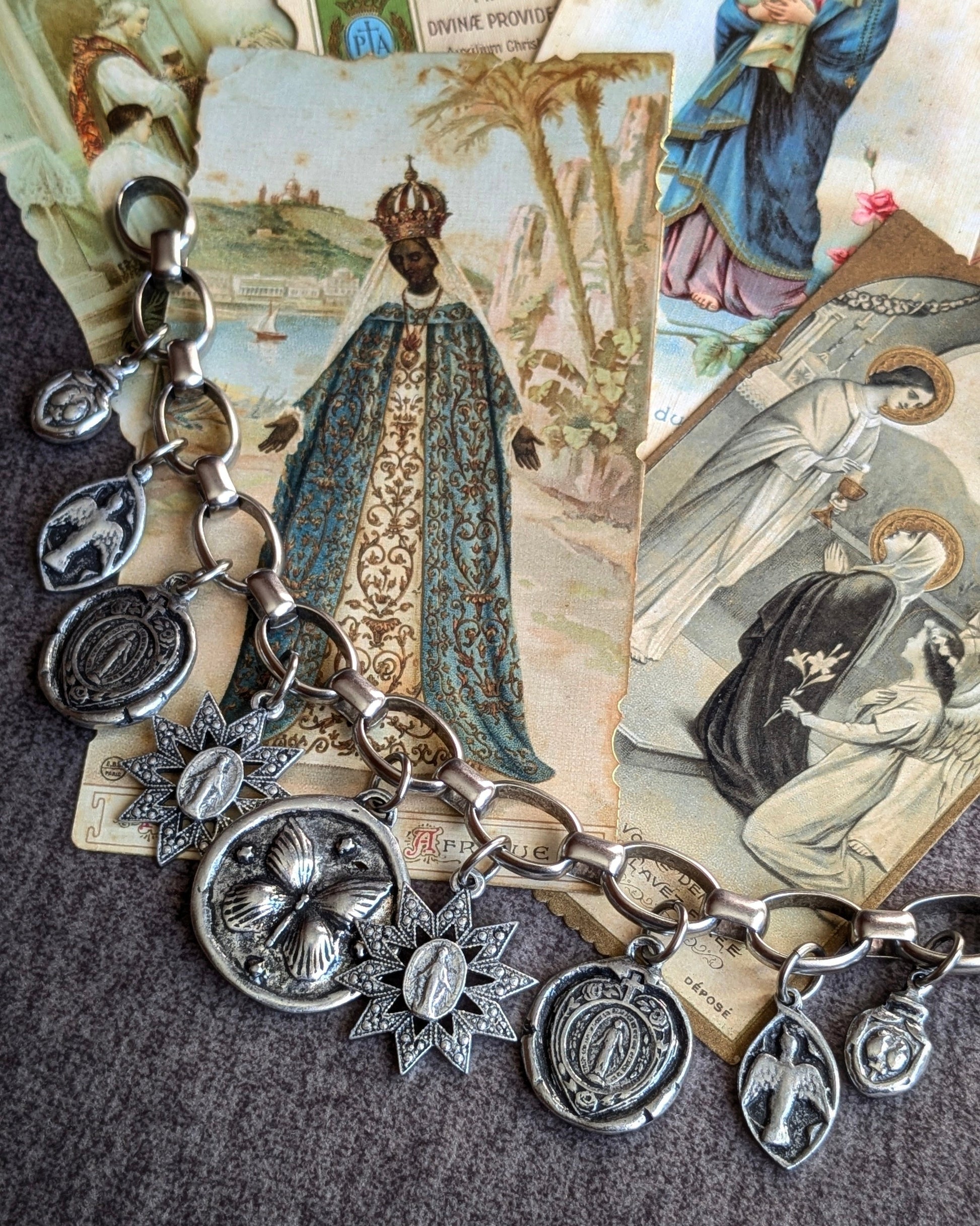 Bracelet ex-voto argenté Ferveur de Mudra avec accumulation de 9 médailles religieuses double face dont Milagros, colombes et croix sur chaîne épaisse.