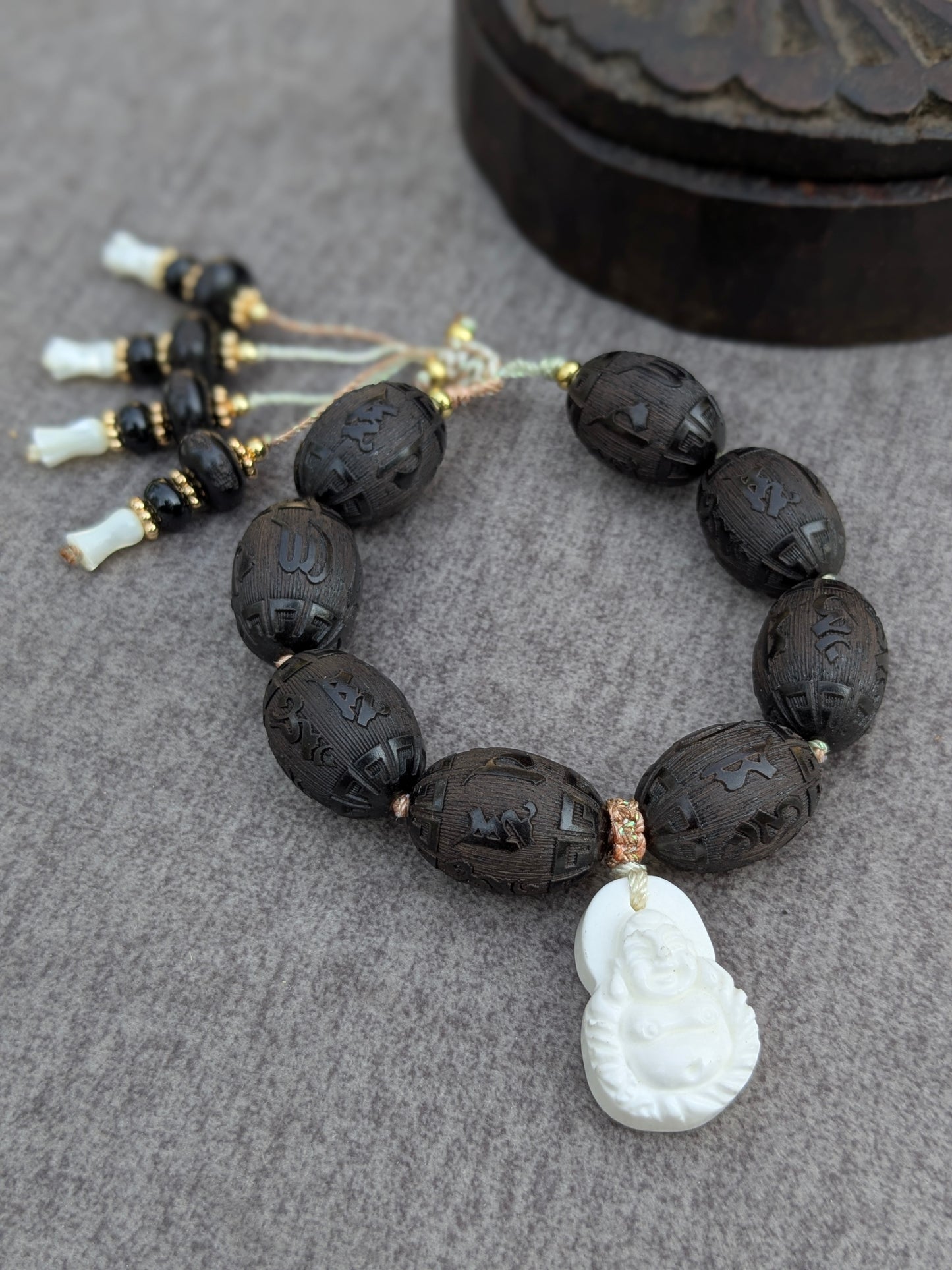 Bracelet Chenrezi Mudra posé sur une boîte ancienne, vue d'ensemble des perles gravées et des pampilles en santal, onyx et nacre