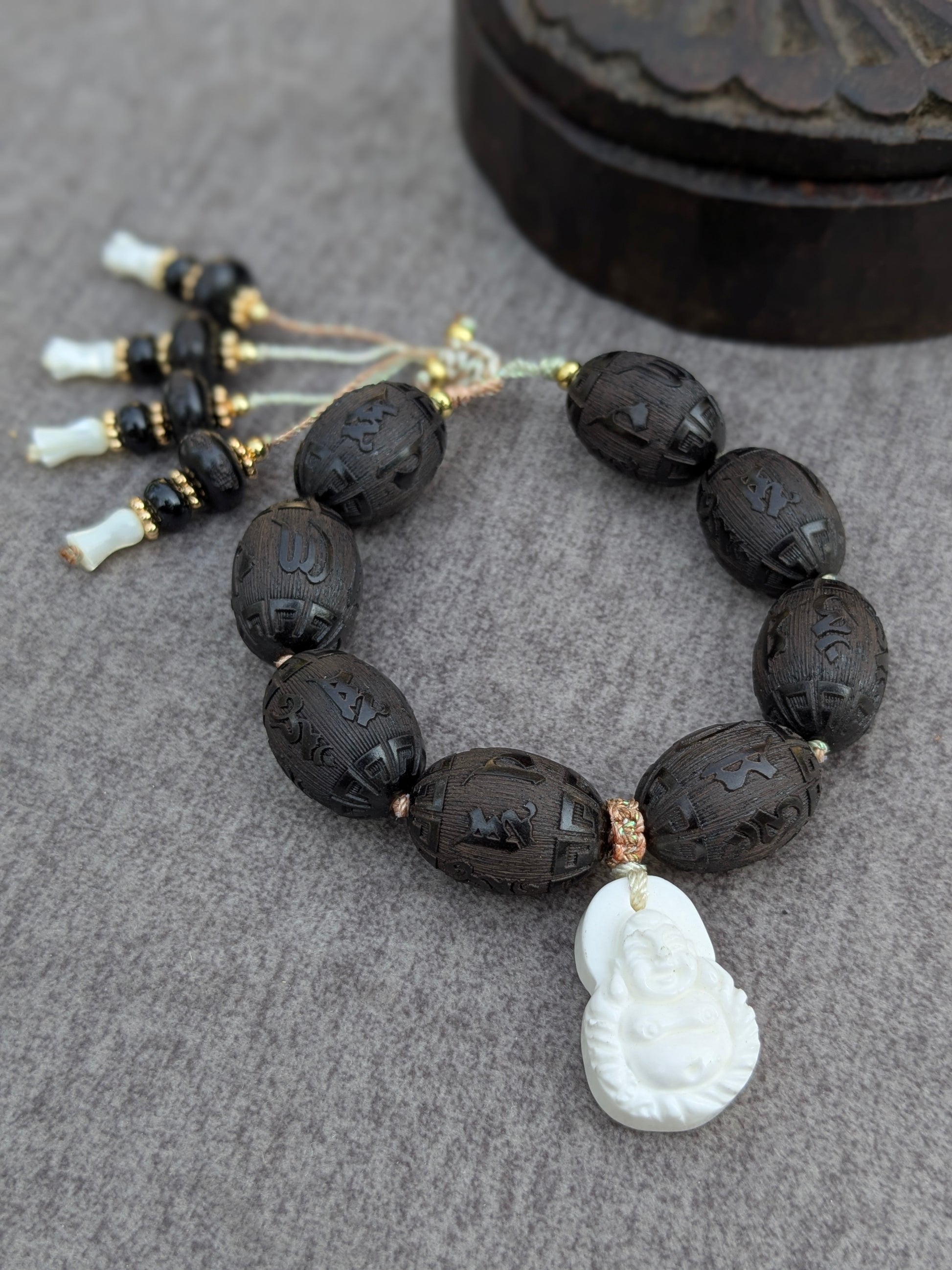 Bracelet Chenrezi Mudra posé sur une boîte ancienne, vue d'ensemble des perles gravées et des pampilles en santal, onyx et nacre