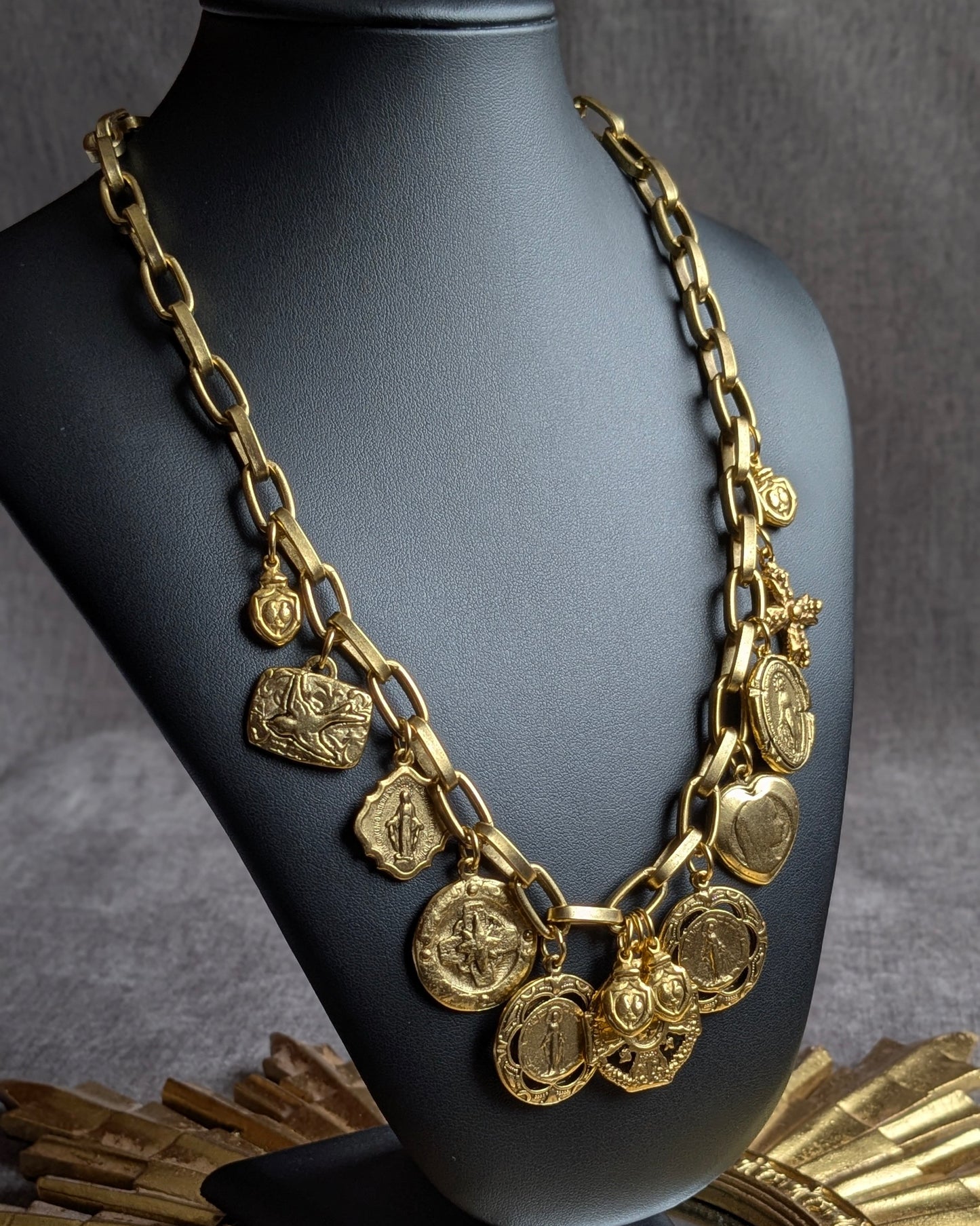 Détail des breloques du collier Miracolo : médaille miraculeuse double face, milagro cœur enflammé et hirondelle dorée sur maillons épais.