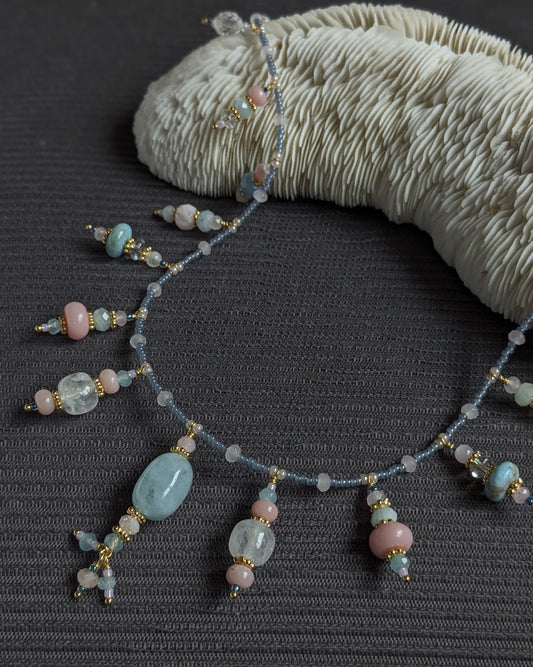 Collier Suryani 64 cm, ras de cou long en pierres fines : béryl bleu, larimar, aventurine bleue, aigue-marine, cristal de roche, opale rose, jade mauve, ponctué de rocailles japonaises givrées bleues.