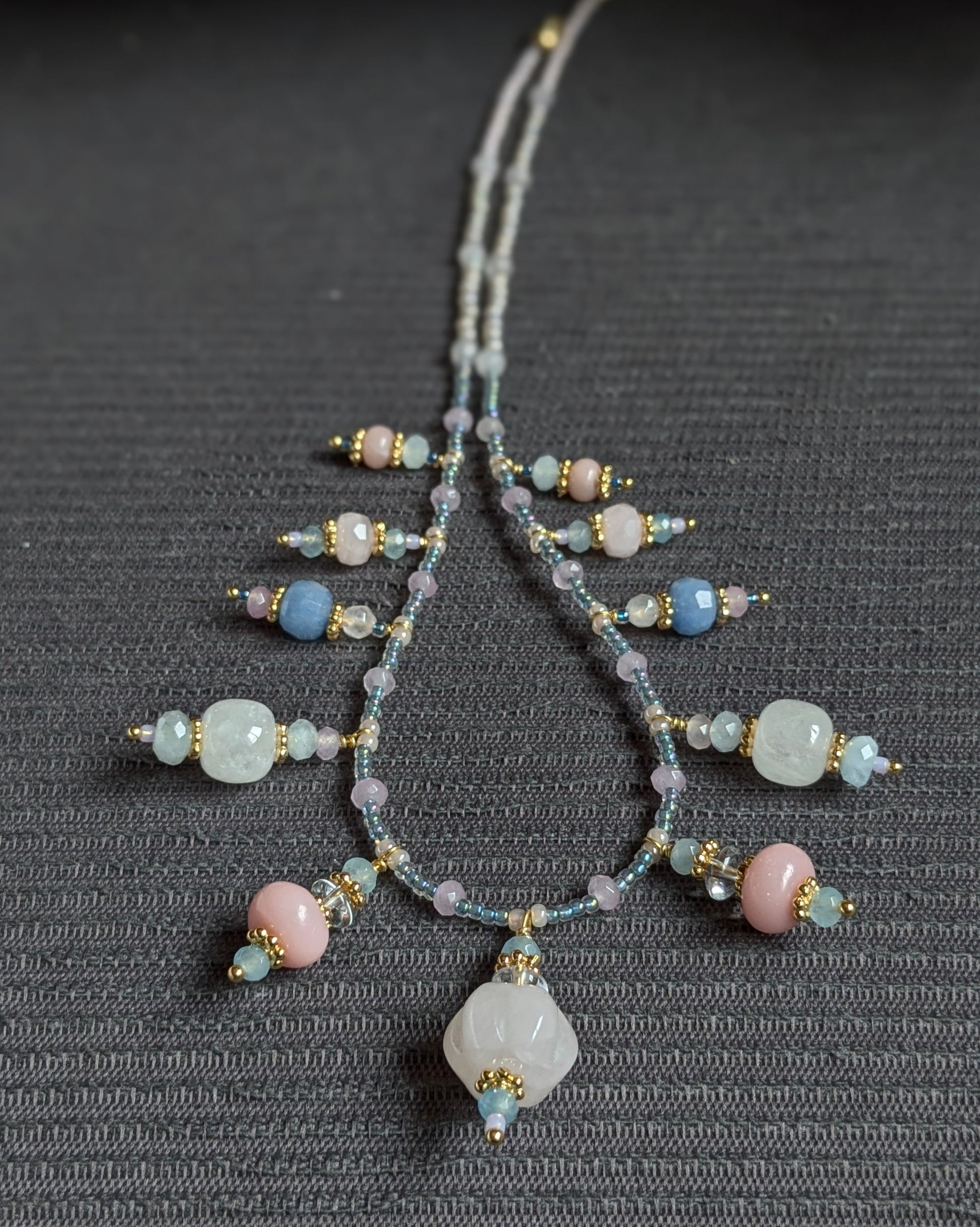 Harmonie de minéraux bleus et roses pour le collier unique Tanisha, présenté sur un support naturel.