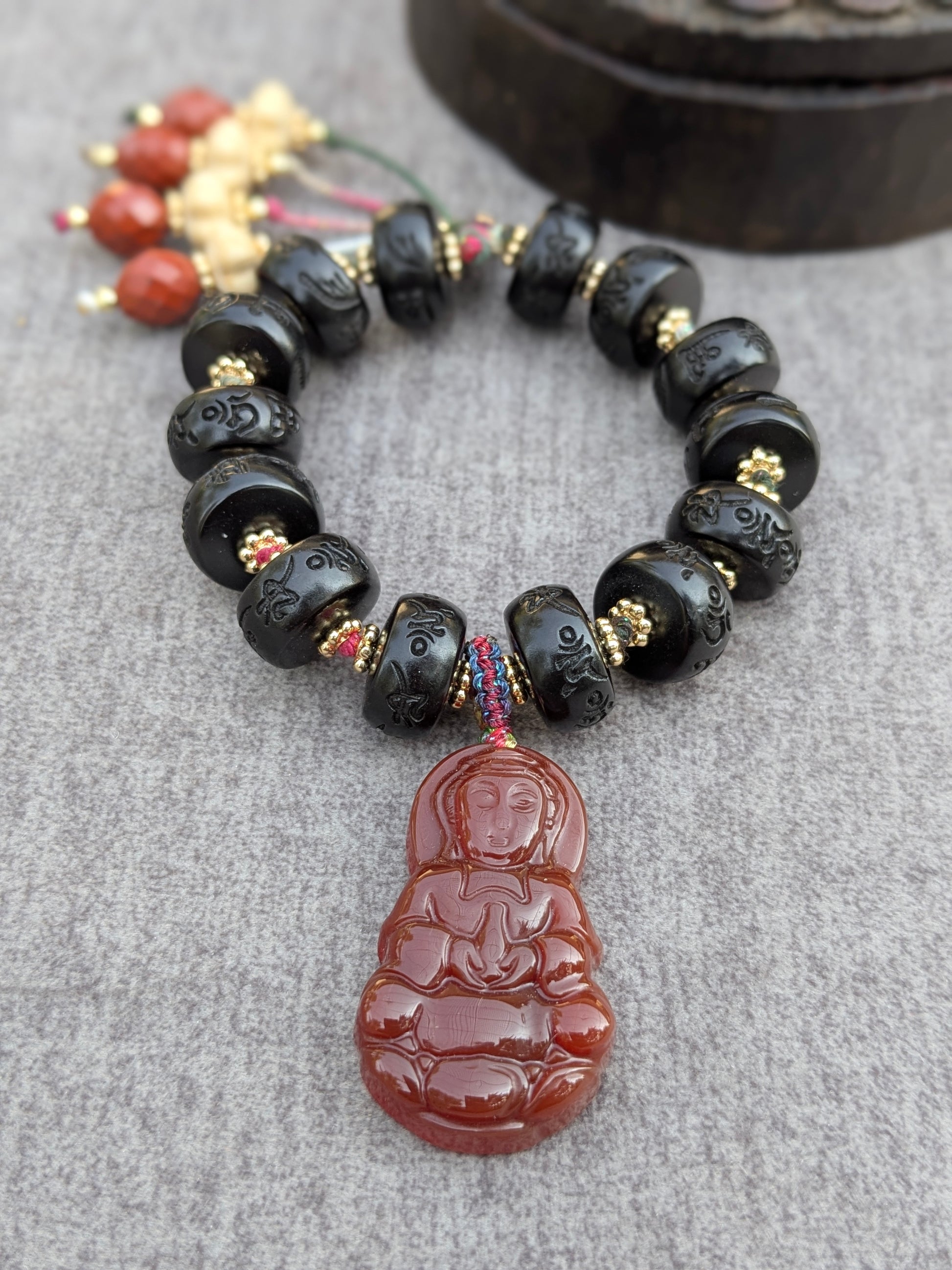 Bracelet Dolma Mudra posé sur une boîte ancienne, vue d'ensemble des perles gravées et des pampilles multicolores
