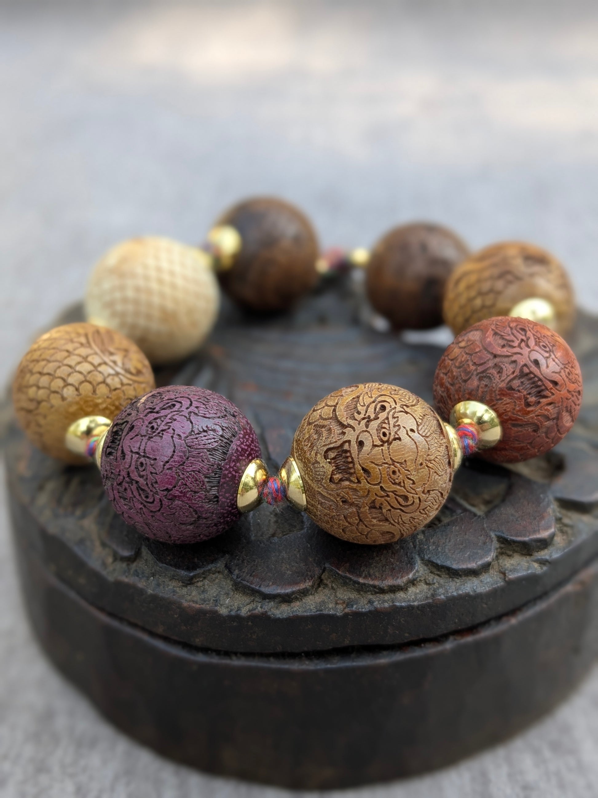 Bracelet Druk Mudra, perles oversize en bois ciselé multicolore gravées de dragons, posé sur une boîte ancienne
