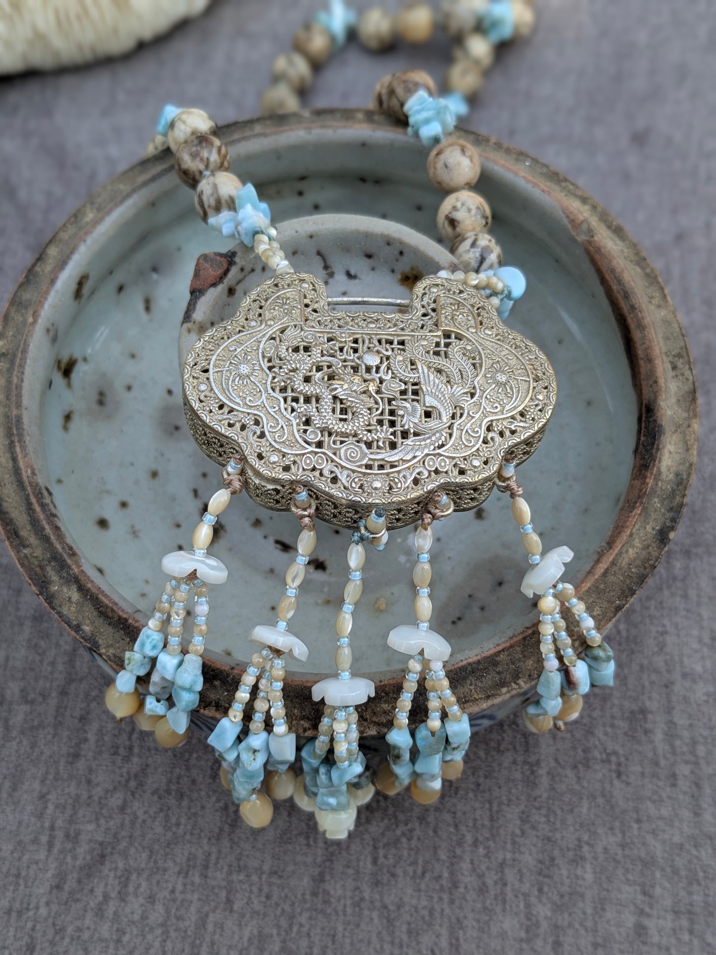 Détail du locket He He posé dans un bol en grès ancien, tassel nacre et larimar visible