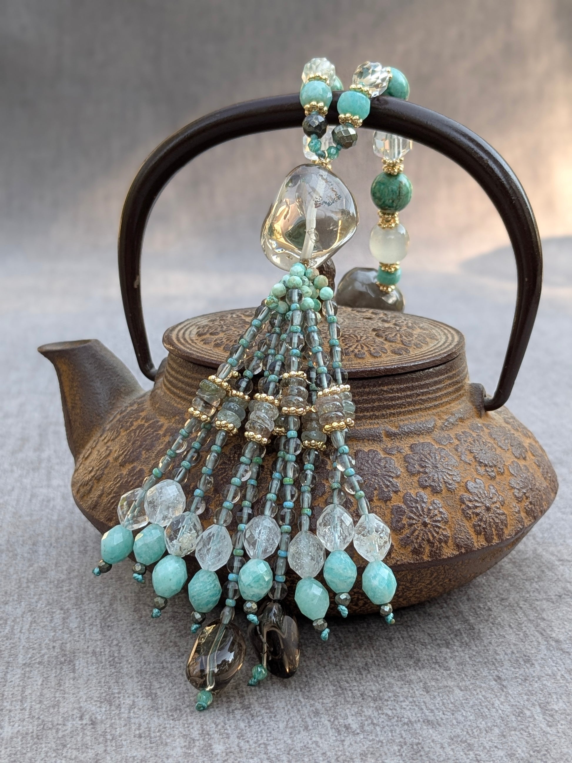 Détail du tassel Nilaya en quartz fumé, quartz fantôme et amazonite, posé sur une théière en fonte