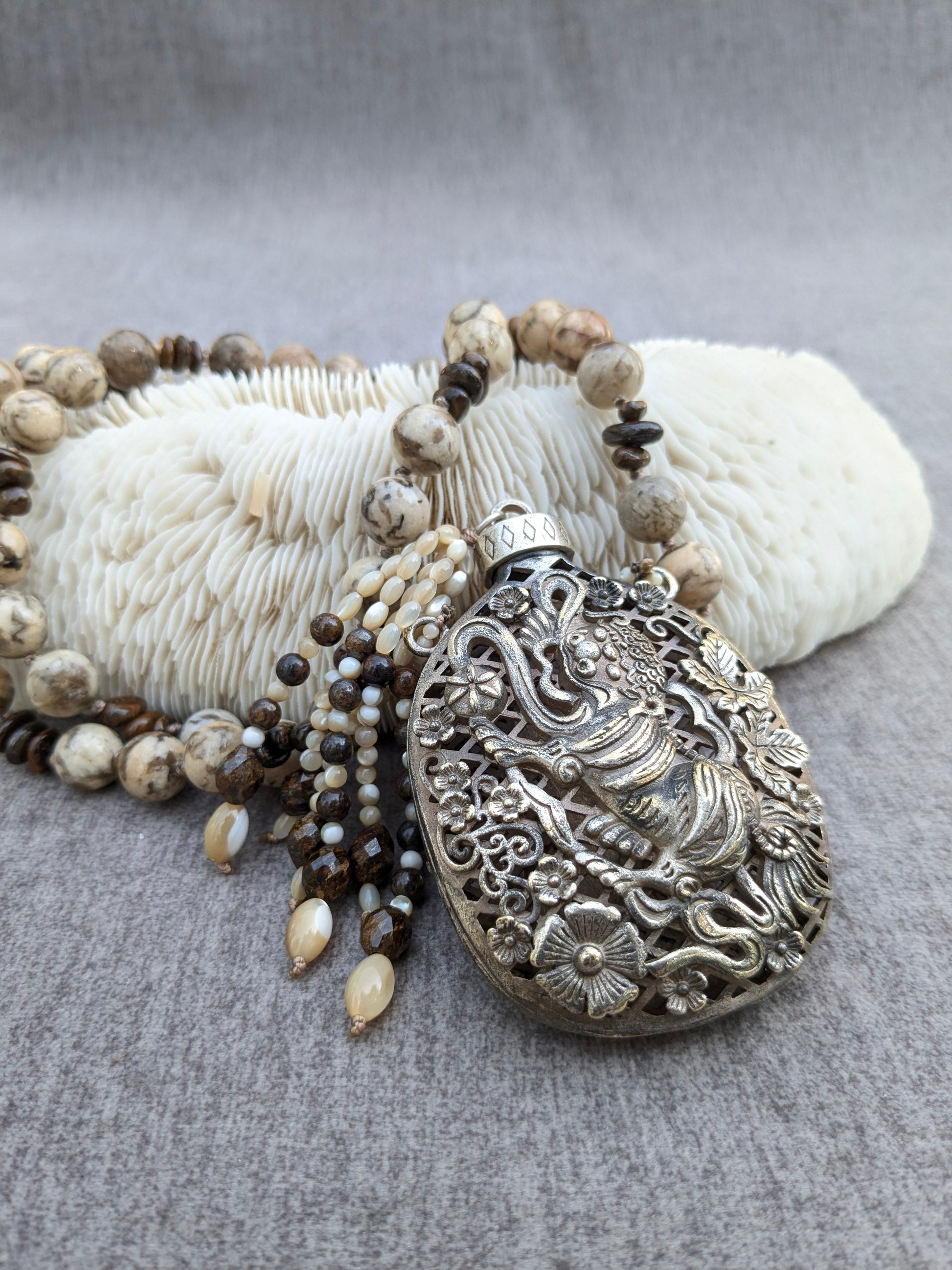 Collier pendentif Shishi en alliage vintage avec perles de feldspath vanilla brown et bronzite, posé sur corail blanc